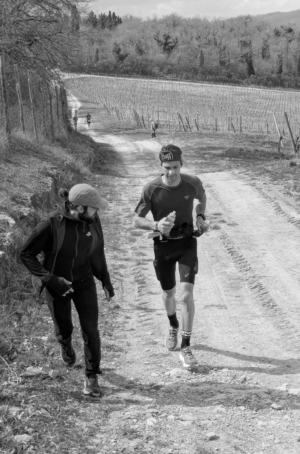 Gabriele durante un allenamento trail running, in affiancamento a un atleta su uno sterrato tra i vigneti